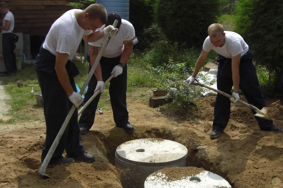 Crew members working around concrete septic system components in an excavated area.