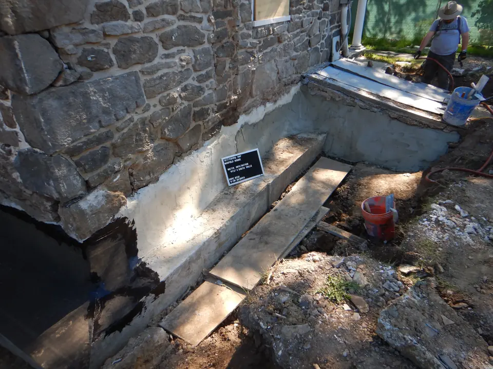 Worker installing a rubber moisture barrier along a repaired masonry foundation footer.